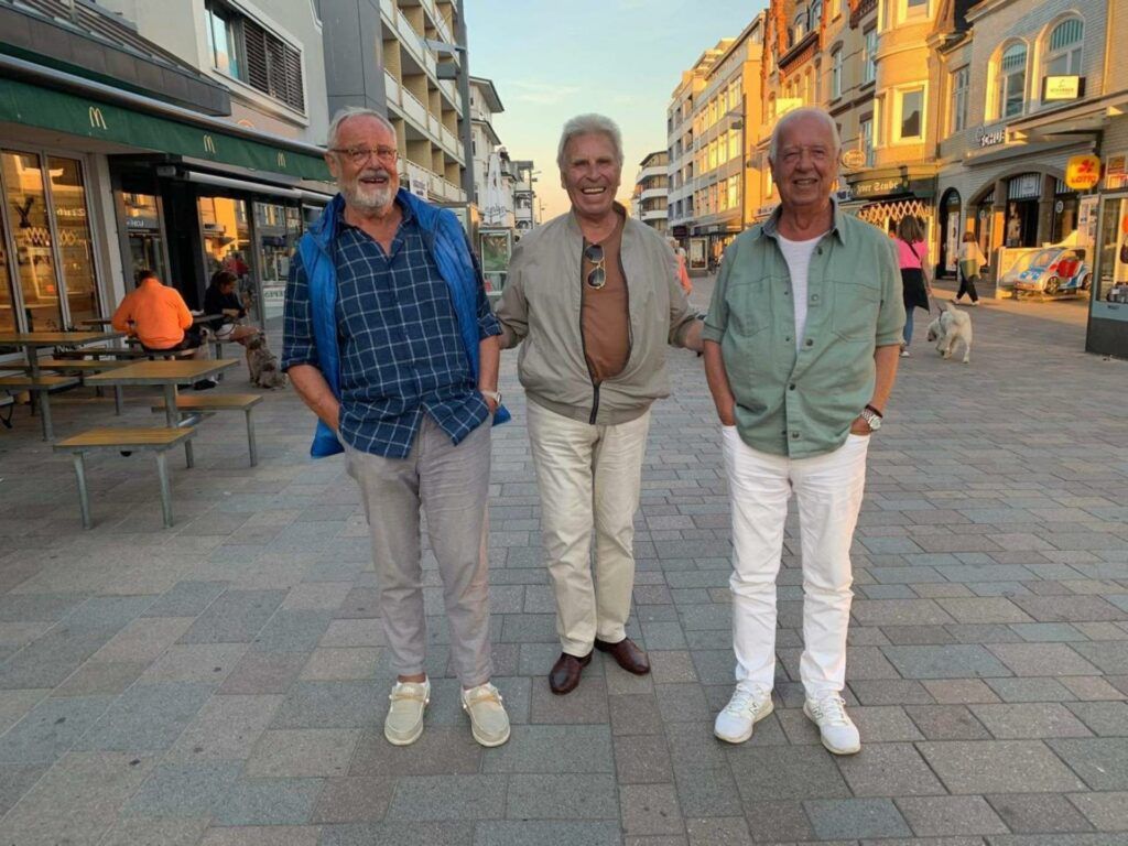 Drei Männer stehen auf einem Bürgersteig in einer Stadt.